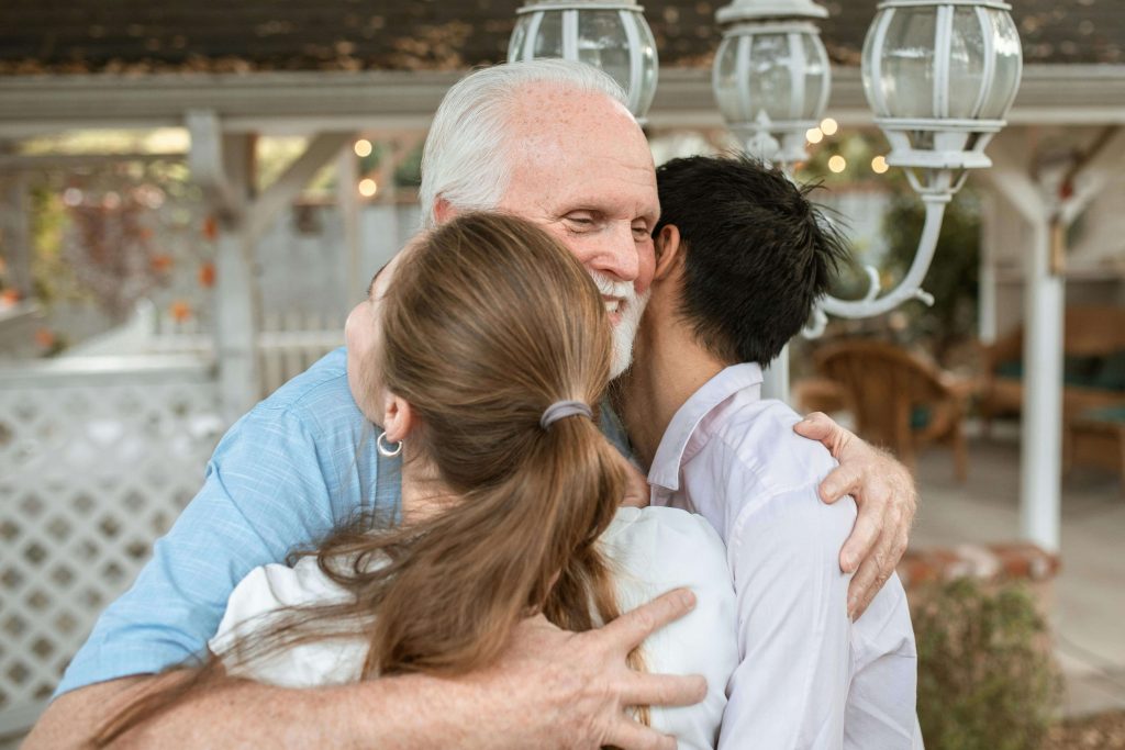 Plano funeral acima de 80 anos. Imagem de um senhor branco abraçando uma mulher e homem jovens.