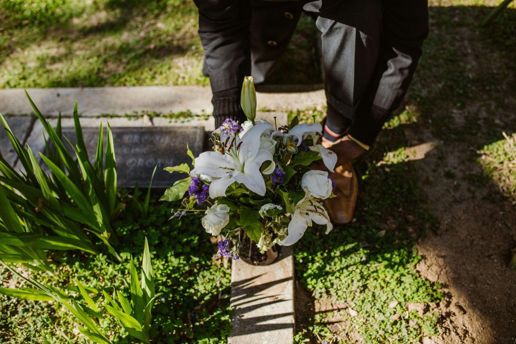 o que é exumação? na imagem aparece um homem colocando flores em cima de um túmulo.